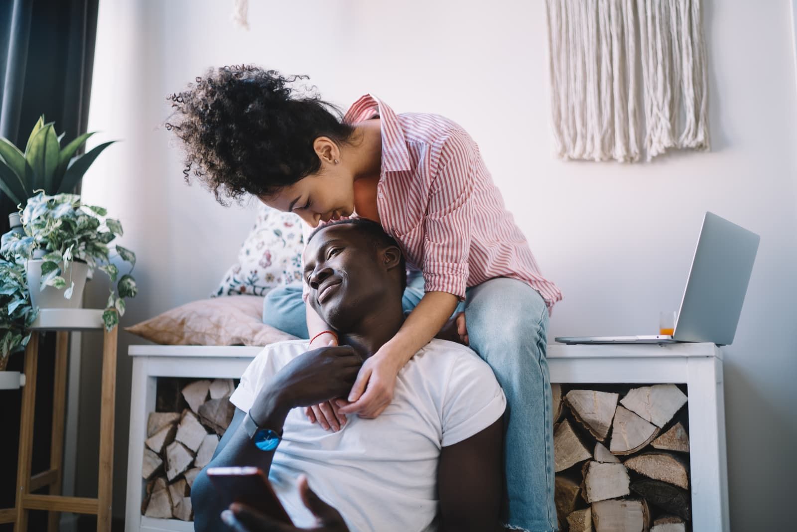 curly woman with bun wearing striped shirt hugging from back and kissing on head man