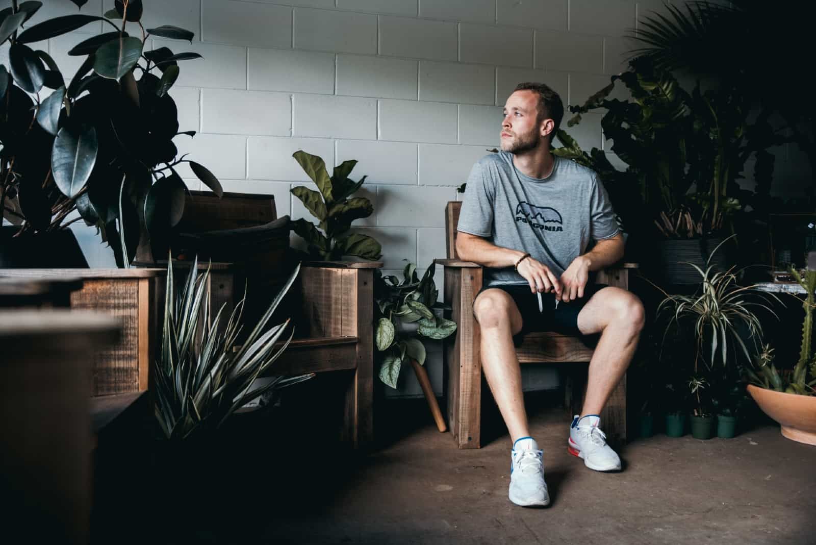 pensive man sitting on chair surrounded with plants