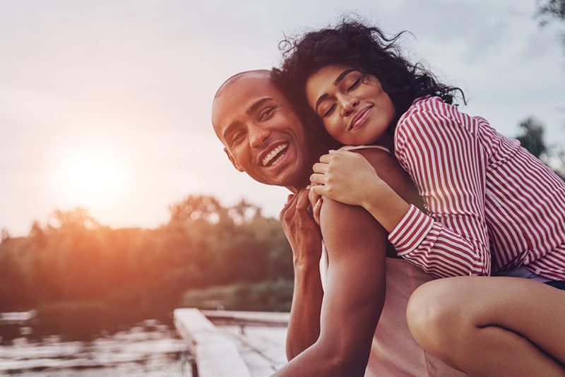 happy woman hugging a man next to the lake