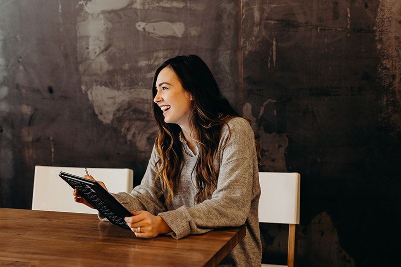 smiling woman sitting at the table holding tablet